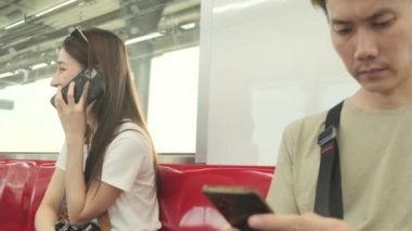 Kameralı güzel Asyalı bayan turist kırmızı koltukta oturur, gökyüzü treniyle seyahat eder, şehir manzarasında taşınırken cep telefonuyla konuşur, tren yoluyla şehir yolcusu yaşam tarzı, iyi yolculuklar..