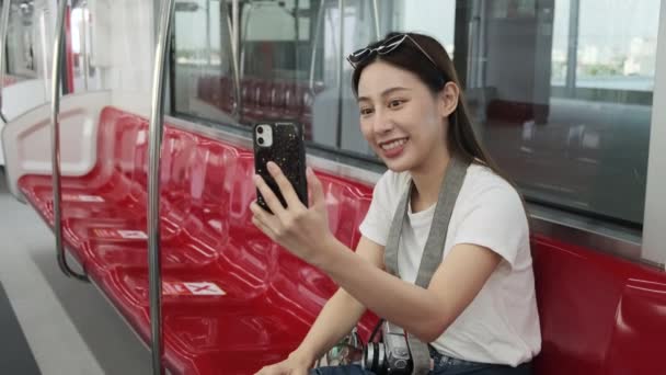 若い美しいアジアの女性観光客オンラインチャット 携帯電話のビデオ通話 チェックイン ソーシャルメディア投稿 旅行都市鉄道輸送 都市旅客ライフスタイル 幸せな旅行休暇旅行 — ストック動画