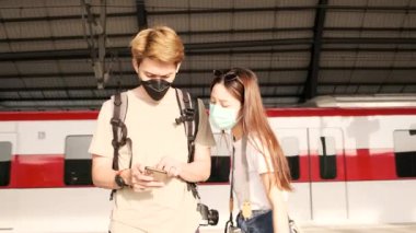 Yüz maskeli birkaç Asyalı turist arama bilgileri, Tayland 'daki bir tren istasyonunda cep telefonu haritasıyla seyahat yerleri, yolcu yaşam tarzı, günlük ulaşım, seyahat tatili. 
