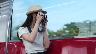 Yüz maskeli güzel Asyalı kadın turist kırmızı koltukta oturur, trenle seyahat eder, fotoğraf çeker, banliyöde seyahat eder, tren yoluyla yolcu yaşamının tadını çıkarır, iyi yolculuklar..