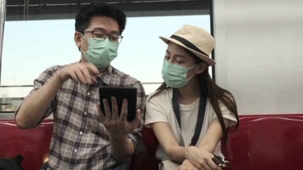 若い顔のマスクカップルアジアの観光客の検索情報 旅行場所を見つけるタブレットマップで電車のキャビン 旅行休暇のライフスタイル カジュアル輸送 旅行休暇タイ — ストック動画