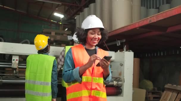アフリカ系アメリカ人女性労働者の安全制服とハード帽子のチャット携帯電話 カメラと笑顔を探して 製紙製造工場の産業機械の機械監督 — ストック動画