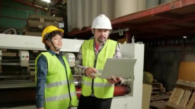 Güvenlik görevlileri ve sanayi mühendisleri makineleri kontrol etmek için dizüstü bilgisayar kullanıyorlar. İki profesyonel kağıt fabrikasında çalışıyor, üretim ekipmanlarını koruyorlar..
