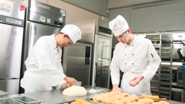 白いコックの制服とエプロンの2人のプロのアジアの男性シェフは ペストリー生地と卵を練り パンと新鮮なベーカリーフードを準備し レストランのステンレス製のキッチンでオーブンで焼く — ストック動画