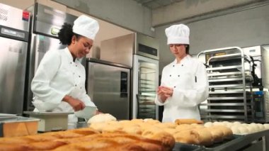  İki profesyonel aşçı üniforması ve önlüklü kadın aşçı hamur ve yumurta yoğurur, ekmek, kurabiye ve taze fırın yemeği hazırlar, bir restoranın paslanmaz çelik mutfağında fırında pişirir..