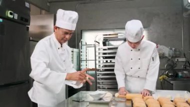 Beyaz aşçı üniforması ve önlükleri içinde iki profesyonel Asyalı şef hamur ve yumurta yoğuruyor, ekmek ve taze fırın yemekleri hazırlıyor, restoranın paslanmaz çelik mutfağında fırında pişiriyorlar..