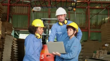 Endüstri fabrikası çalışanları güvenlik üniforması ve hard hat ile depolamayı dizüstü bilgisayarla kontrol ediyorlar depoda stok siparişleri, karton istifleme kartonlarını forklift ile dolduruyorlar, ürün lojistiği üretiyorlar..