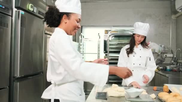 白いコックの制服とエプロンの2人のプロの女性シェフは ペストリー生地と卵を練り クッキー 焼きたてのベーカリーフードを準備し レストランのステンレス製のキッチンでオーブンで焼く — ストック動画