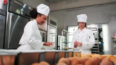 İki profesyonel aşçı üniforması ve önlüklü kadın aşçı hamur ve yumurta yoğurur, ekmek, kurabiye ve taze fırın yemeği hazırlar, bir restoranın paslanmaz çelik mutfağında fırında pişirir..