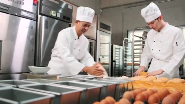 两名身穿白色厨师制服和围裙的亚洲专业厨师正在揉搓糕点面团和鸡蛋 准备面包和新鲜烘焙食品 并在餐馆的不锈钢厨房烘焙 — 图库视频影像
