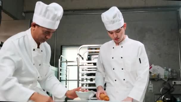 两名身穿白色厨师制服和围裙的亚洲专业厨师正在揉搓糕点面团和鸡蛋 准备面包和新鲜烘焙食品 并在餐馆的不锈钢厨房烘焙 — 图库视频影像
