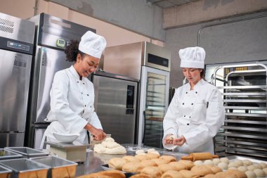 İki profesyonel aşçı üniforması ve önlüklü kadın aşçı hamur ve yumurta yoğurur, ekmek, kurabiye ve taze fırın yemeği hazırlar, bir restoranın paslanmaz çelik mutfağında fırında pişirir..