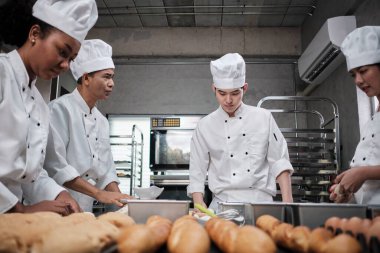 Çok ırklı profesyonel gurme takımı, beyaz aşçı üniforması ve önlüklü dört şef hamur ve unu yoğurur, ekmek ve fırın yemeği hazırlar, paslanmaz çelik restoran mutfağında fırında pişirir..