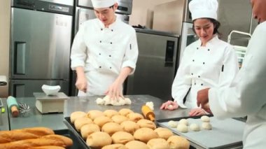 Profesyonel gurme takımı, beyaz aşçı üniforması ve önlüklü üç genç aşçı hamur ve yumurta yoğurur, ekmek ve taze fırın yemeği pişirir paslanmaz çelik restoran mutfağında fırında pişirir..