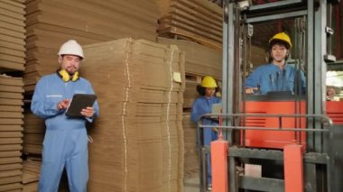 Endüstri fabrikası çalışanları güvenlik üniforması ve hard hat ile depolamayı dizüstü bilgisayarla kontrol ediyorlar depoda stok siparişleri, karton istifleme kartonlarını forklift ile dolduruyorlar, ürün lojistiği üretiyorlar..