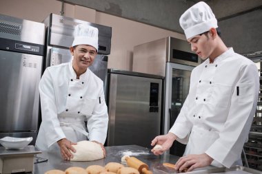 Beyaz aşçı üniforması ve önlükleri içinde iki profesyonel Asyalı şef hamur ve yumurta yoğuruyor, ekmek ve taze fırın yemekleri hazırlıyor, restoranın paslanmaz çelik mutfağında fırında pişiriyorlar..