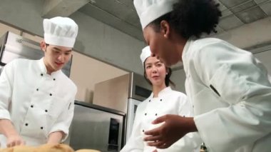 Profesyonel gurme takımı, beyaz aşçı üniforması ve önlüklü üç genç aşçı hamur ve yumurta yoğurur, ekmek ve taze fırın yemeği pişirir paslanmaz çelik restoran mutfağında fırında pişirir..