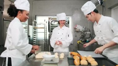 Profesyonel gurme takımı, beyaz aşçı üniforması ve önlüklü üç genç aşçı hamur ve yumurta yoğurur, ekmek ve taze fırın yemeği pişirir paslanmaz çelik restoran mutfağında fırında pişirir..