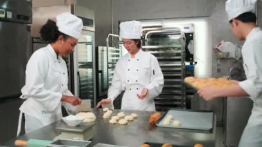 Profesyonel gurme takımı, beyaz aşçı üniforması ve önlüklü üç genç aşçı hamur ve yumurta yoğurur, ekmek ve taze fırın yemeği pişirir paslanmaz çelik restoran mutfağında fırında pişirir..