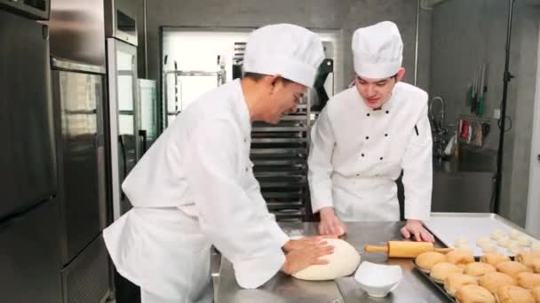 白いコックの制服とエプロンの2人のプロのアジアの男性シェフは ペストリー生地と卵を練り パンと新鮮なベーカリーフードを準備し レストランのステンレス製のキッチンでオーブンで焼く — ストック動画
