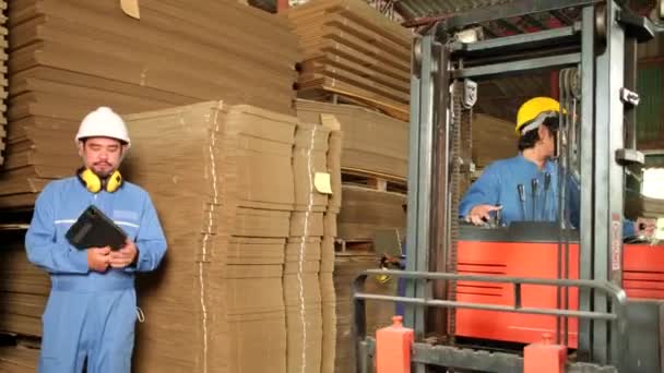 工业工厂工人穿着安全制服 头戴硬礼帽 用笔记本电脑检查存储情况 仓库里的库存订单 用叉车堆放纸板箱的管理堆栈 制造产品物流 — 图库视频影像
