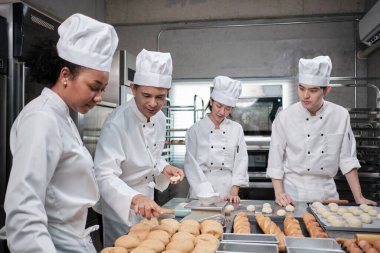 Çok ırklı profesyonel gurme takımı, beyaz aşçı üniforması ve önlüklü dört şef hamur ve unu yoğurur, ekmek ve fırın yemeği hazırlar, paslanmaz çelik restoran mutfağında fırında pişirir..