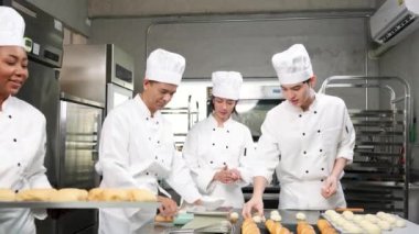 Çok ırklı profesyonel gurme takımı, beyaz aşçı üniforması ve önlüklü dört şef hamur ve yumurta yoğurur, ekmek ve fırın yemeği hazırlar, paslanmaz çelik restoran mutfağında fırında pişirir..