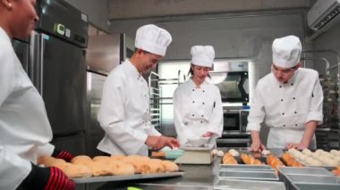Çok ırklı profesyonel gurme takımı, beyaz aşçı üniforması ve önlüklü dört şef hamur ve yumurta yoğurur, ekmek ve fırın yemeği hazırlar, paslanmaz çelik restoran mutfağında fırında pişirir..