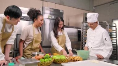 Mutfak kursu, aşçı üniformalı kıdemli erkek aşçı genç aşçılık sınıfı öğrencilerine hamur yoğurmayı ve rulo yapmayı öğretiyor, fırın yemekleri için malzemeler hazırlıyor, paslanmaz çelik mutfakta meyveli turtalar pişiriyor..