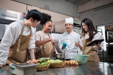 Hobi mutfak kursu, aşçı üniforması giyen kıdemli erkek aşçı, genç aşçılık sınıfı öğrencilerine hamur işleri için malzeme hazırlamayı, karıştırmayı ve karıştırmayı, paslanmaz çelik mutfakta meyveli turta yapmayı öğretiyor..
