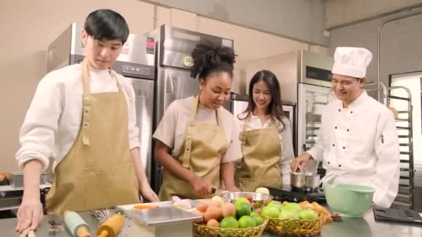 趣味の料理コース 料理の制服を着た上級男性シェフは 若い料理クラスの学生にリンゴの皮をむいて切ること ペストリー料理の材料 レストランのステンレススチールキッチンのフルーツパイを教えています — ストック動画