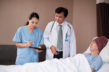 Professional doctors team in uniform health check Asian recovery male patient by stethoscope, medicine treatment at inpatient room bed in hospital ward, medical clinic, cancer examination consult.