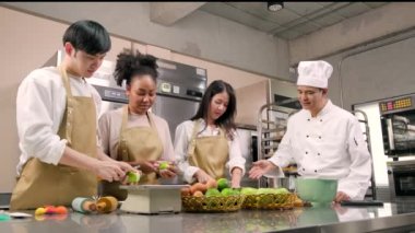 Hobi mutfak kursu, aşçı üniforması giyen kıdemli aşçı genç aşçılık sınıfı öğrencilerine elma soymayı ve doğramayı öğretiyor. Hamur işleri için malzemeler, paslanmaz çelik mutfakta meyveli turtalar..