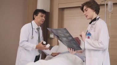 Üniformalı doktorlar röntgen filmlerini tartışıyor, Asyalı iyileşme hastalarına hastane koğuşundaki yataklı odada yatan erkek hastalara, tıbbi kliniğe, kanser muayenesine,.