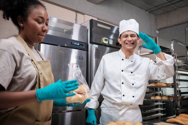 Üniformalı ve eldivenli iki profesyonel şefin portresi. Neşeli, gururlu gülümsemeli ve mutfaktaki ekmekle dalga geçiyor. Ticari hamur işlerinin ve taze fırın mutfağının ortağı..