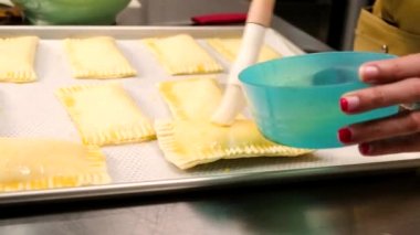 Bir aşçının ellerinin önlükle yakın plan fotoğrafı yumurta sarısından pasta fırçasına karamel kremi, sonra da fırça ile pasta ve fırın yemeği pişirmeden önce aşçılık kursunun mutfağında..