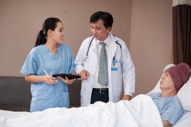 Üniformalı profesyonel doktorlar Asyalı erkek hastayı steteskopla kontrol ediyor, hastane koğuşundaki yatağında ilaç tedavisi görüyor, tıbbi klinik, kanser muayenesi....