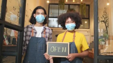 Yeni başlayan iki genç barista partneri, COVID-19 'dan sonra kafeterya işlerinde çalışırken maske takıp, mutlu ve neşeli gülümsemelerini takınıp, açık yazı yazıp, tabelayı gösteriyorlar..