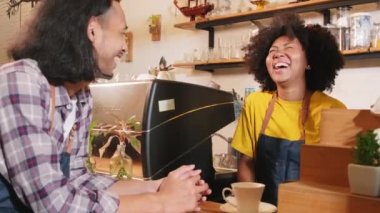 İki kafe işletme ortağı ve arkadaşları, Afro-Amerikan kadın ve Taylandlı erkek barmenler kahve dükkanının tezgahında birlikte neşeli bir gülümseme, mutlu servis işi ve KME girişimcisi.