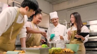 Hobi mutfak kursu, aşçı üniforması giyen kıdemli erkek aşçı, genç aşçılık sınıfı öğrencilerine hamur işleri için malzeme hazırlamayı, karıştırmayı ve karıştırmayı, paslanmaz çelik mutfakta meyveli turta yapmayı öğretiyor..