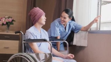 Üniformalı genç Asyalı kadın terapist, hastane yatağında kemoterapi gördükten sonra iyileşme ve motivasyon için tekerlekli sandalyeli erkek hastayı teşvik ediyor..