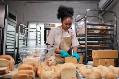 Fırın küçük bir iş kurma teslimatı. Afro-Amerikalı bir kadın aşçı el yapımı ekmek ve taze hamur işlerini kutulara koyup mutfaktan online müşteri alışverişi için gönderiyor..