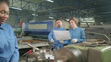 Güvenlik üniforması giyen profesyonel endüstri işçileri ve mühendislerin ortakları metal iş araçlarıyla çalıştılar, torna makinelerinin mekanik çizimini tartıştılar ve imalat fabrikasındaki atölyelerde çalıştılar.