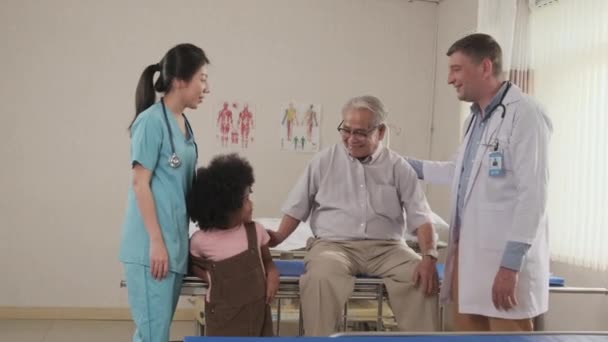 白人男性医師と女性看護師が話し合い 高齢者の祖父 回復した患者 そして彼の孫娘 病院病棟のベッドを訪れる多人種家族に肯定的な気分でいじめる — ストック動画