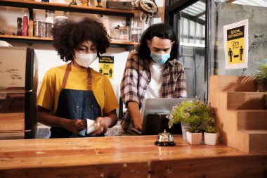 İki genç kafe ortağı ve önlüklü girişimciler bir kahve dükkanında maske takıyor, yeni normal bir yaşam tarzında işe başlıyor COVID19 pandemik karantinasının KOBİ iş etkisi.