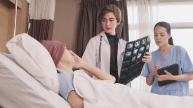 Üniformalı beyaz kadın doktor, Asyalı radyologla röntgen filmini ve iyileşen erkek hastayı hastane koğuşunda yatağında, tıbbi klinikte ve kanser muayenesinde açıklıyor..