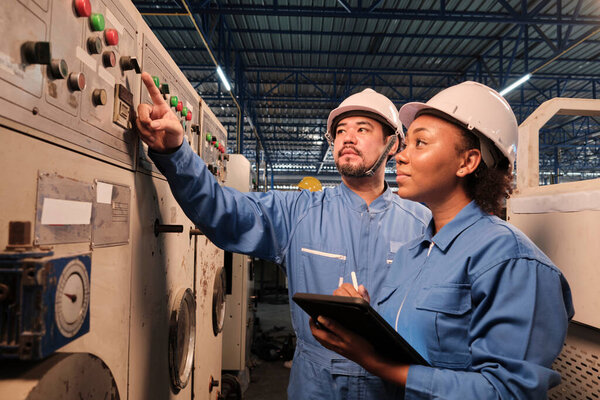 Профессиональный промышленный инженер-партнер в жестких шляпах и униформе безопасности инспектировать панель управления машины, техническое обслуживание с планшетом на заводе механического производства, электротехническое обслуживание занятости.