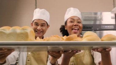 Beyaz üniformalı profesyonel şeflerin portresi kameraya neşeli bir gülümsemeyle bakıyor ve mutfakta bir tepsi ekmekle gurur duyuyor. Pastane yemekleri ve taze günlük fırın işlerinden bir arkadaş ve ortak..