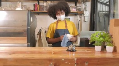 Afro-Amerikalı bayan barista kahve fincanlarını temizler, kafenin penceresinden bakar, yeni normal yaşam tarzı servisinde müşterileri bekler, COVID-19 salgın karantinasının KOBİ iş etkisi.