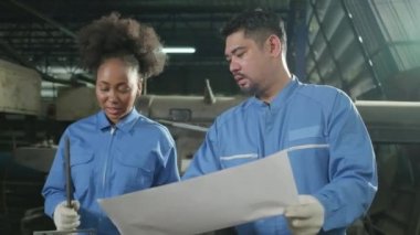 Güvenlik üniforması giyen iki profesyonel endüstri çalışanı ve mühendis ortakları metal iş araçlarıyla çalıştılar, torna makinelerinin mekanik çizimini tartıştılar ve imalathanede atölye çalışmalarını tartıştılar..